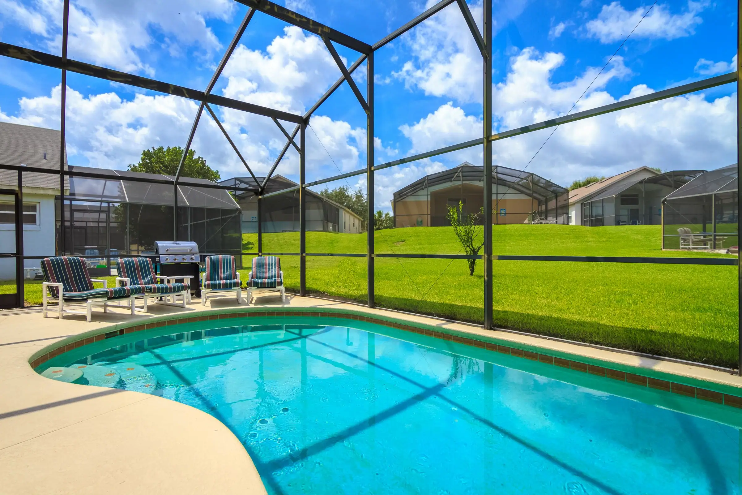 Screened lanai pool with a paved deck, chairs and a grill in Florida